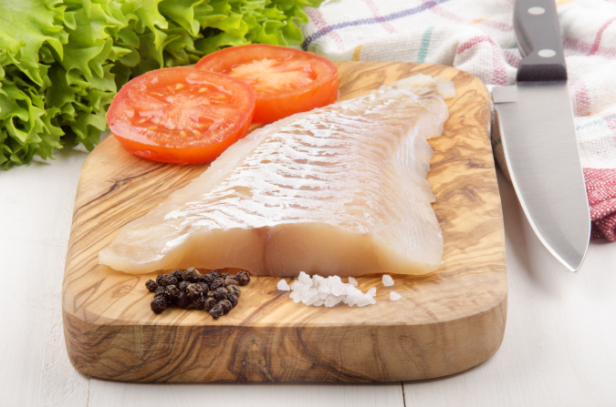 Haddock fillet on cutting board with salt and pepper